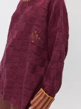 Pullover de punto jacquard con diseño de cuadros en relieve, cuello alto y mangas largas. Presenta detalles de pespuntes en color rojo en el cuello y los puños, aberturas laterales y logo bordado en el pecho.