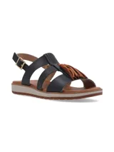 Sandalia de cuero negro con diseño de tiras, detalle de flecos en color tostado sobre el empeine y cierre con hebilla metálica dorada en el tobillo. Cuenta con una suela plana y flexible en tonos beige y marrón.