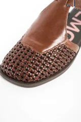 Sandalias de cuero marrón, con puntera cerrada de diseño trenzado, empeine liso y tira ajustable con hebilla en el talón. Cuenta con suela plana y baja.