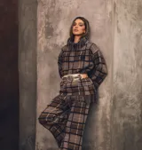 Sweater oversize de lana natural, color marrón con estampado cuadrillé en negro, blanco y azul. Presenta cuello alto y detalles de flecos torneados en el ruedo.