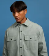 Camisa manga larga de sarga en color verde militar, con cuello inglés, cierre frontal de botones negros y dos bolsillos con solapa en el pecho.