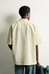 Camisa de corte regular fit color amarillo con rayas verticales blancas, cuello solapa, manga corta, bolsillo de parche en el pecho y cierre frontal con botones.