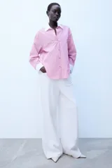 Camisa de rayas rosas y negras, con cuello solapa y puños anchos en color blanco. Presenta mangas largas, bajo asimétrico y cierre frontal con botones.