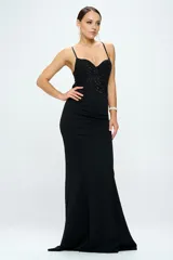 Vestido largo de fiesta color negro, con cuerpo tipo corset estructurado adornado con lentejuelas y perlas, escote corazón y breteles finos. La falda es de corte sirena, entallada en la cintura y caderas, con caída fluida hasta el suelo.
