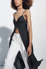 Top largo confeccionado en lino, color negro, con tirantes finos, escote en V con encaje y detalle de frunces y lazada frontal.