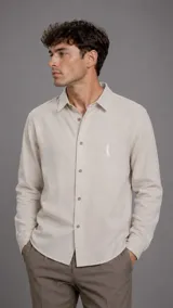 Camisa de lino color beige, de manga larga, con cuello camisero, cierre frontal con botones y bordado sutil en el pecho.