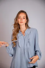 Camisa de color celeste con volados decorativos en el cuello y la parte delantera, cuenta con cordones para ajustar el escote, mangas largas con puños y corte holgado.