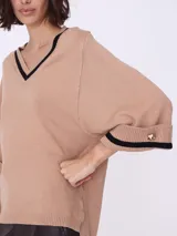 Sweater color beige de tejido de punto, con escote en V con borde negro y mangas 3/4 con puños con detalle de botón dorado.