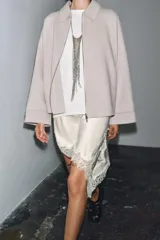 Chaqueta de lana en color beige, con cuello solapa, cierre frontal con cremallera metálica, mangas largas con corte evasé y bajo asimétrico.