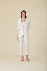 Saco de mujer color crema con diseño estructurado, cierre frontal de un botón dorado y bolsillos laterales con solapa. Presenta mangas tres cuartos con detalle de botones dorados en los puños.