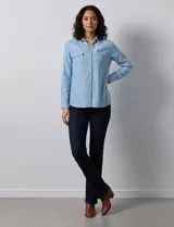 Camisa de manga larga en tela denim de color azul medio, con cuello clásico, botones frontales y dos bolsillos de parche con solapa en el pecho.