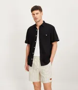 Camisa de hombre de manga corta, color negro, confeccionada en tejido de lino y algodón. Presenta un corte confort, cuello camisero, botonadura frontal y un bolsillo de parche en el pecho.