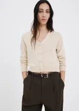 Cardigan de punto color beige, con escote en V y cierre frontal de botones con lazos decorativos.