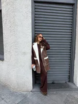 Chaleco largo de eco cuero color marrón con interior y detalles de corderito en solapas y bolsillos frontales.