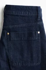 Pantalón de jean color azul oscuro con diseño de pernera ancha, talle alto, bolsillos diagonales al frente y raya marcada planchada en el centro de las piernas.