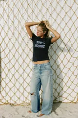Jeans de tiro bajo y corte wide leg, confeccionados en denim de color celeste claro con lavado desgastado. Presentan detalles de roturas y aplicación de tachas metálicas en los laterales y bolsillos delanteros. Cierre frontal con cremallera y botón.