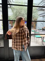 Campera reversible de corte holgado con cuello alto. De un lado presenta un diseño a cuadros en tonos marrones y beige, y del otro lado un diseño liso. Cuenta con cierre frontal de botones y mangas largas.
