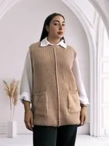 Chaleco largo de punto color beige, con cuello redondo y bolsillos frontales. Diseño sin mangas y corte recto.