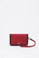 Billetera compacta de Bimba y Lola en color rojo, confeccionada en poliamida con detalles en piel. Presenta un diseño minimalista con el logo metálico de la marca en el frente, cierre de cremallera y una correa de muñeca extraíble a juego.