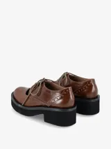 Zapato tipo guillermina con cordones, confeccionado en cuero negro con detalles de perforaciones estilo brogue. Presenta una suela de plataforma gruesa y tacón cuadrado.