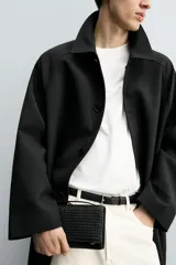 Cartera negra rectangular con diseño trenzado y correa fina para colgar.