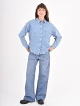 Camisa de jean de corte oversize, con cierre frontal de botones metálicos, cuello clásico y bolsillo frontal decorado con tachas plateadas.