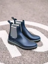 Botas de agua de caña baja color bordó, con elásticos laterales a rayas en tonos burdeos, beige y marrón. Cuenta con suela dentada negra, costuras blancas decorativas en el borde y presilla trasera para facilitar el calce.
