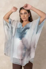 Blusa tipo túnica de gasa semitransparente con escote en V y mangas amplias. Presenta un diseño estampado con efecto acuarela en tonos azules, grises y marrones sobre fondo blanco.