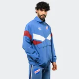 Buzo tipo rompevientos de nylon con medio cierre frontal, cuello alto y puños elásticos. Presenta un diseño en bloques de color azul, blanco y bordó, con el escudo del Club Nacional de Football y el logo de Umbro estampados en el pecho.