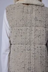 Chaleco tejido de punto color marrón con cuello de piel sintética, cierre frontal con cursor de cuero y diseño acolchado con cortes horizontales.