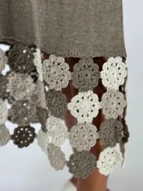 Vestido midi de tejido ligero color beige, con cuello en V, mangas cortas y ruedo decorado con aplicaciones de crochet en tonos tierra y rosado.