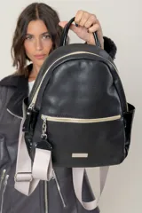 Mochila de cuero vacuno con textura granulada, color negro, con cierre frontal y bolsillos laterales. Cuenta con correas de cinta ajustables en color gris claro y herrajes metálicos dorados.