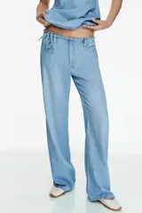 Pantalón de jean estilo pijamero de tiro medio, con cintura elástica ajustable mediante cordones. Presenta corte recto, bolsillos laterales y cierre frontal con cremallera y gancho metálico.
