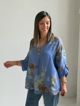 Blusa azul de lino con estampado floral en tonos marrones y verdes, escote en V con botón decorativo grande y mangas largas holgadas con puños arremangables.