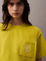 Remera corta color amarillo con cuello redondo, mangas cortas y bolsillo en el pecho con escudo bordado en blanco.