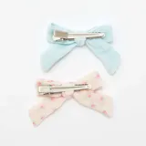 Pack de dos pinzas para el pelo con forma de moño, una celeste lisa y otra color crema con estampado de flores rosas.