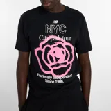 Remera de algodón de corte holgado con cuello redondo y mangas cortas. Presenta un estampado frontal gráfico con el logo de la marca, la inscripción NYC City park tour y un diseño floral en color rosado.