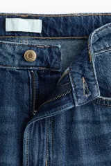 Jean de tiro alto con corte wide leg, confeccionado en denim de algodón rígido. Presenta diseño clásico de cinco bolsillos, cierre frontal con botón y acabado de lavado azul medio con efecto desgastado.
