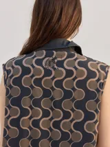 Vestido midi camisero sin mangas, de corte recto y holgado. Cuenta con cuello camisero liso en color naranja y cierre frontal parcial con botones. Presenta un estampado geométrico psicodélico en tonos naranja y beige.