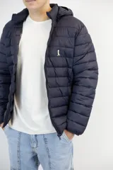 Campera puffer de nylon color azul marino, liviana y con capucha desmontable. Presenta cierre frontal y logo bordado en el pecho.
