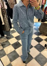 Conjunto de camisa y pantalón de denim celeste con estampado de rosas en tono claro. La camisa es de manga larga con cuello y cierre frontal con botones. El pantalón es de corte recto con bolsillos laterales y traseros.