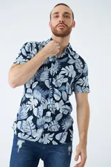 Camisa de manga corta con estampado botánico de hojas en tonos azul y blanco. Presenta cuello clásico, cierre frontal abotonado y corte slim.