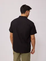 Camisa de manga corta color negro, con cuello clásico y cierre frontal de botones.