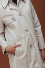 Trench de cuero ovino, de largo midi, con cuello clásico, cierre frontal de botones y diseño de líneas limpias.