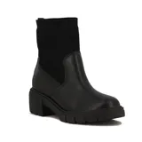 Bota Beira Rio de caña media, color negro, con cuerpo de cuero sintético y caña de tejido elástico acanalado. Cuenta con taco bloque de 4 cm y suela track dentada.