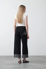 Pantalón de denim negro de corte recto y pierna amplia, con largo al tobillo. Presenta bordados florales en color blanco en la parte frontal superior y en la botamanga.