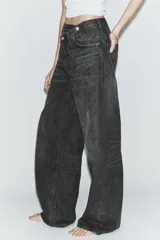 Jeans de tiro alto con diseño de pierna ancha y corte extra largo. Presenta una cintura cruzada asimétrica con cierre de cremallera y botones metálicos, además de un diseño clásico de cinco bolsillos.