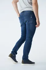 Pantalón de jean corte regular, color azul oscuro, con diseño de cinco bolsillos, pasacintos y detalles de roturas localizadas en la parte frontal.