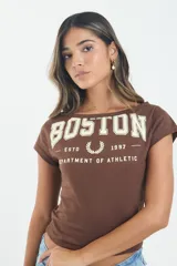 Remera corta color marrón con cuello bote y mangas cortas. Presenta un estampado frontal estilo universitario con la palabra 'BOSTON' y el texto 'ESTD 1997 DEPARTMENT OF ATHLETIC' junto a un logo de laureles.