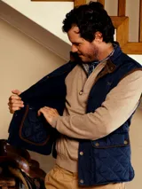 Chaleco acolchado de diseño capitoneado con cierre frontal de botones a presión y bolsillos delanteros con solapa. Presenta un cuello alto y un corte clásico.